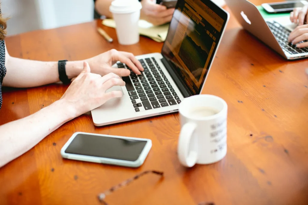 Mains au clavier d’un ordinateur portable sur un bureau en bois, tasse et téléphone