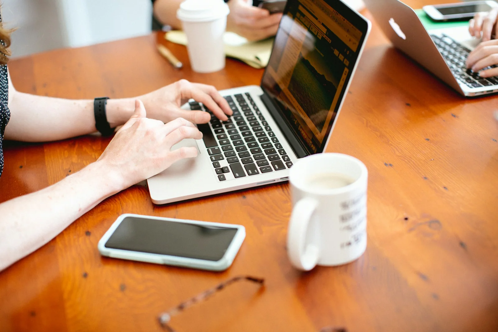 Mains au clavier d’un ordinateur portable sur un bureau en bois, tasse et téléphone